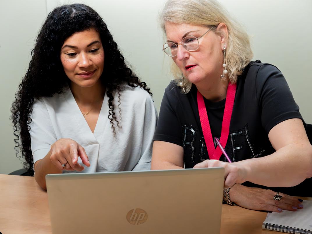 2 vrouwen zitten aan tafel en wijzen naar een laptop