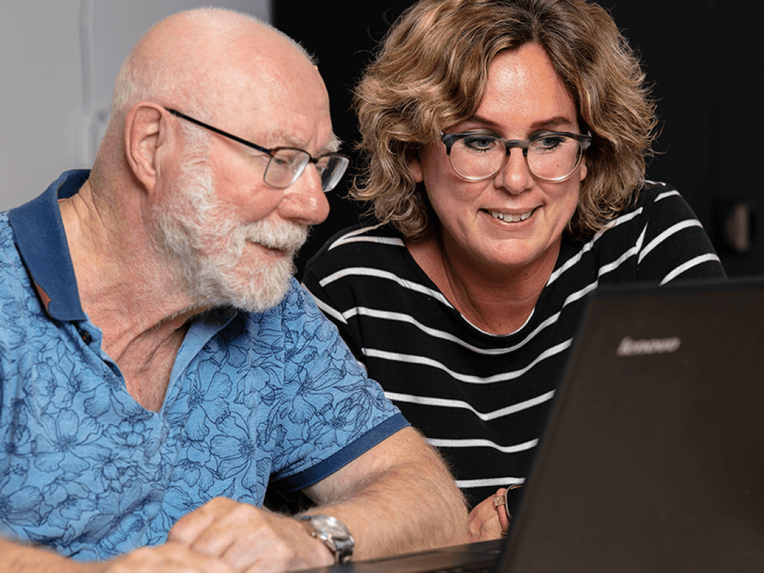 Man en vrouw zitten achter de laptop en de vrouw kijkt mee of helpt met de meneer