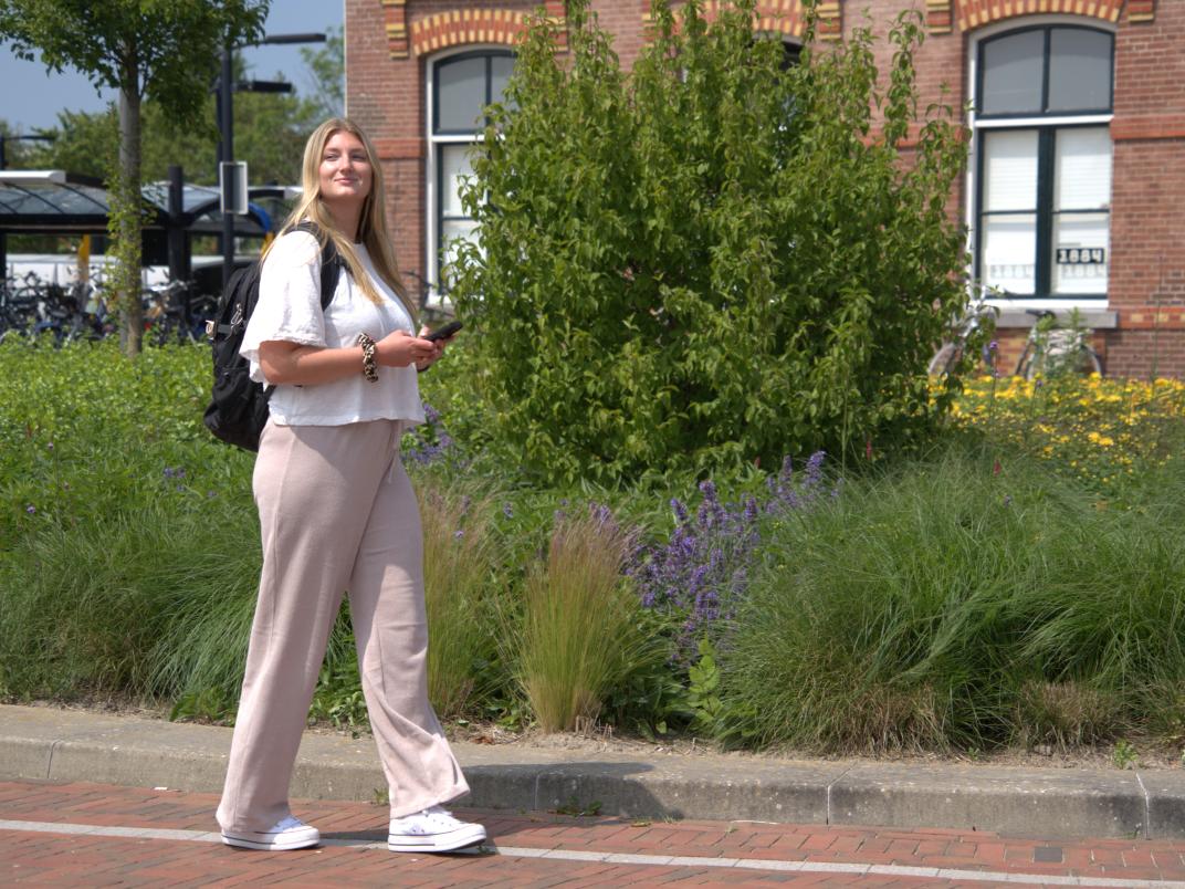 Vrouw loopt buiten en heeft haar telefoon vast en een rugzak op